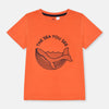 Child wearing an orange t-shirt with a whale graphic and text on a beige background