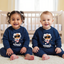 Two children wearing matching navy blue sweaters with astronaut graphics in a nursery.