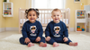 Two children wearing matching navy blue sweaters with astronaut graphics in a nursery.