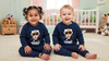 Two children wearing matching navy blue sweaters with astronaut graphics in a nursery.