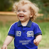 Child wearing a blue sports shirt with text, standing outdoors.
