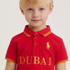 Child wearing a red polo shirt with 'Dubai' printed on it against a plain background