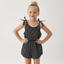 Young girl wearing a black and white polka dot romper with bow straps on a white background