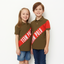 Two children wearing matching brown polo shirts with red 'Team Polo' stripes on a white background.