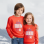 Two children wearing matching red sweatshirts with text on a white background