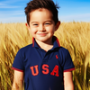 Child wearing a blue polo shirt with 'USA' on it, standing in a wheat field.