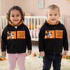 Two children wearing matching black hoodies with orange designs in a nursery.