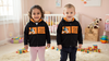 Two children wearing matching black hoodies with orange designs in a nursery.