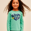 Young girl wearing a teal long-sleeve shirt with a heart design on a beige background