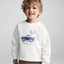 Child wearing a white sweatshirt with a blue truck graphic and text on a gray background