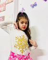 Young girl wearing a white long-sleeve top with a gold snowflake design on a plain background