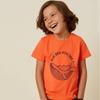 Child wearing an orange t-shirt with a whale graphic and text on a beige background