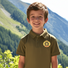 Young boy wearing a green polo shirt with a logo, standing in front of a mountainous landscape.