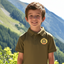 Young boy wearing a green polo shirt with a logo, standing in front of a mountainous landscape.