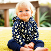 Child wearing a navy blue hoodie with white floral patterns sitting on yellow grass.