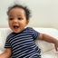 Baby wearing a navy and white striped shirt sitting on a white couch.