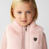 Young girl wearing a pink fur vest with a heart emblem on a light gray background