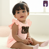 Baby wearing a pink outfit with text, sitting on a white surface.