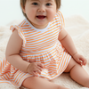 Baby wearing an orange and white striped dress sitting on a soft surface