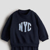 Child wearing a navy blue sweatshirt with 'NYC' in light blue letters on a beige background